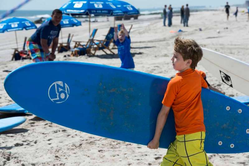 A boy holds a surfboard at the beach