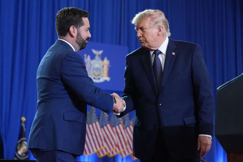Rep. Mike Lawler shakes hands with President Donald Trump onstage at Rockland Community College, with American flags in the background